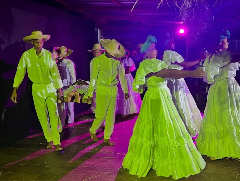 Dancers in bright green costumes on the festival stage at night.